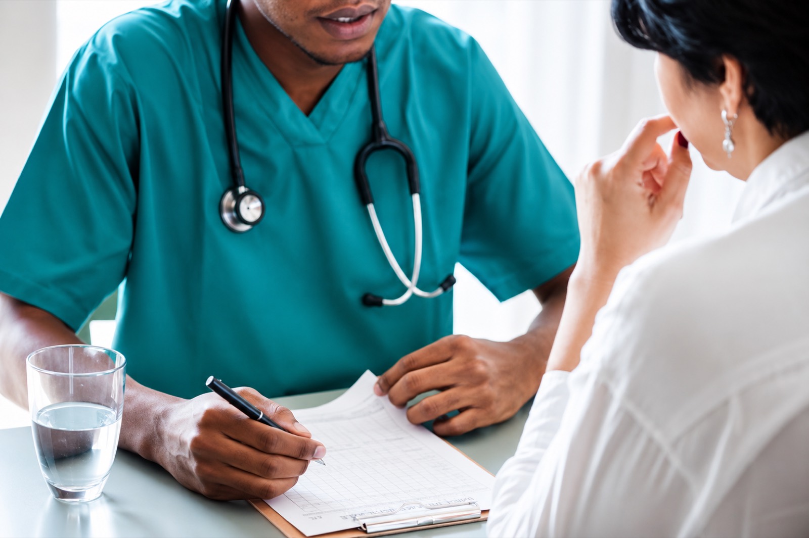 Médico registrando o plano de tratamento junto à paciente em consulta